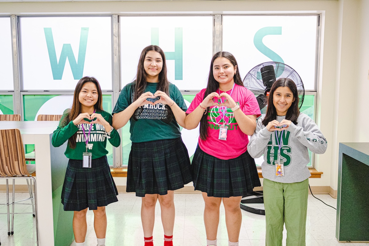 four school girls smiling and making a heart sign