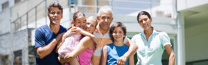 Family smiling outside modern house, parents, senior grandparents and children