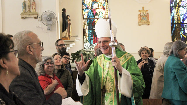 Archbishop Gustavo signing "Love" to parishioners at Mass