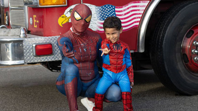 Man and child dressed as Spiderman posing in front of a firetruck