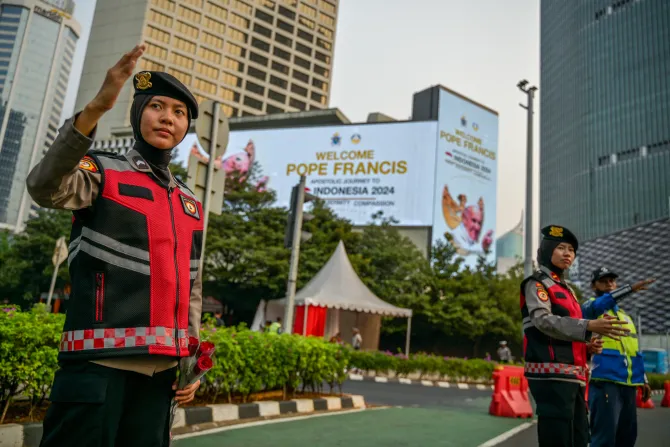 Indonesian police direct traffic next to billboards displaying a welcome message for Pope Francis in Jakarta