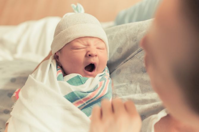 A yawning baby bundled in a blanket