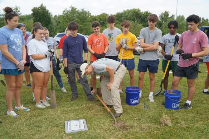 Ben Kresse, a theology teacher at St. Xavier High School, shows a group of students how to uncover a temporary marker on a gravesite