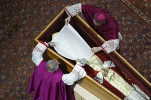 Archbishop Georg Gänswein and Monsignor Diego Giovanni Ravelli place a white veil over the late pope’s face